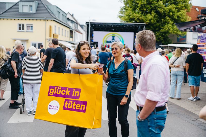 Frau mit einer riesigen bedruckten Tüte spricht mit Passanten.